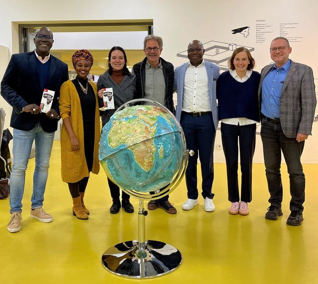 Sieben Personen stehen hinter einem großen Globus, mehrere halten Programmhefte der Afrikatage in den Händen